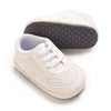 A pair of cream-colored baby pre-walker sneakers with a gray textured sole and white laces.