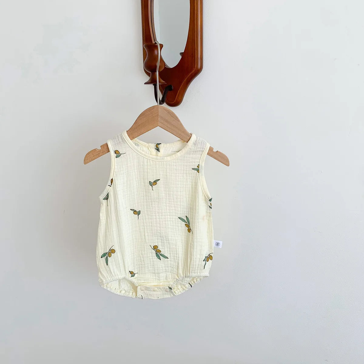 A cream-colored baby cotton sleeveless jumpsuit bodysuit set hanging on a wooden hanger.