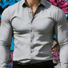 A male model wearing a gray long-sleeve formal shirt and black trousers against a colorful graffiti background.
