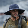 A man wearing a dark bucket hat and a green t-shirt with a backpack in an outdoor setting.