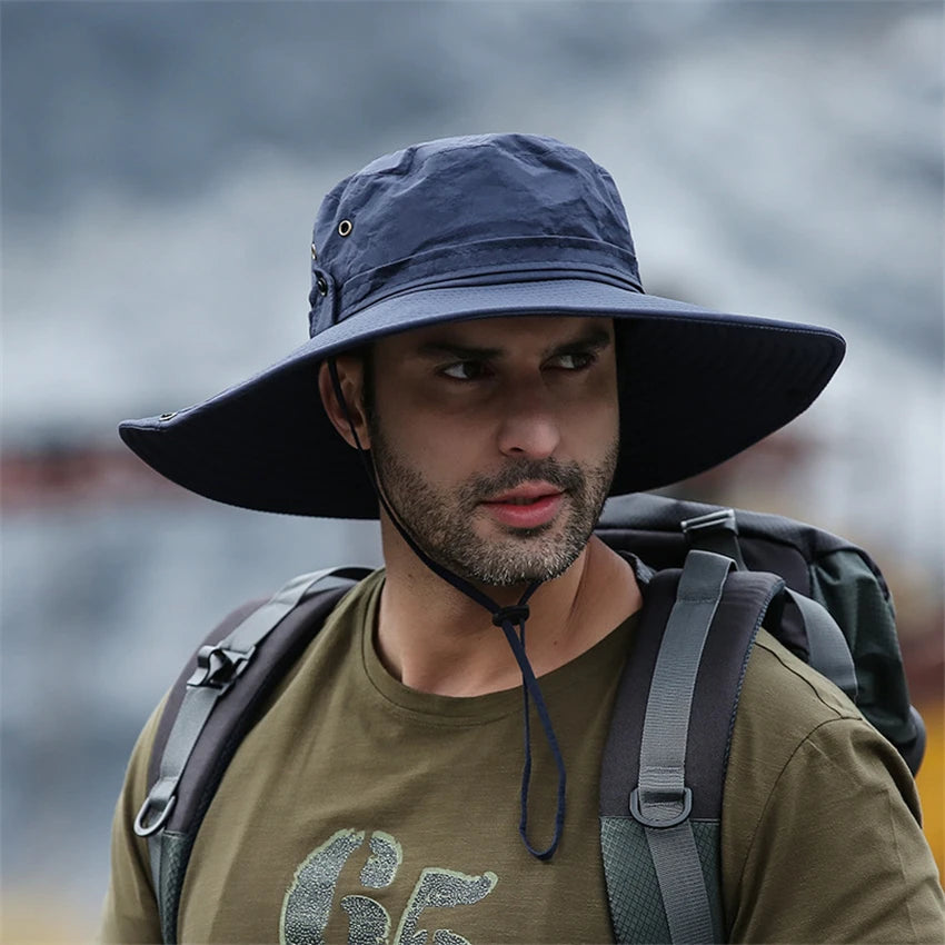 A man wearing a dark bucket hat and a green t-shirt with a backpack in an outdoor setting.