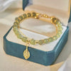 Bracelet double couche en perles de jade vert clair avec pendentif feuille, dans une boîte bleu canard.