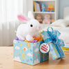 A white bunny plush toy is sitting in a colorful gift box decorated with clouds and stars.