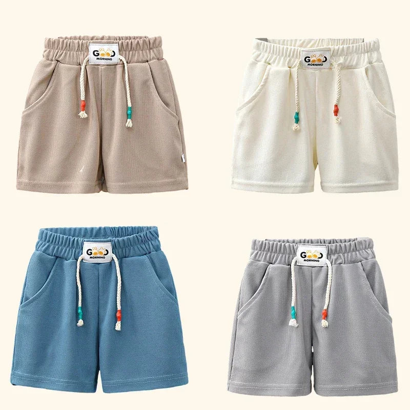 A set of three kids beach shorts in beige, cream, and blue colors with elastic waist and drawstrings.