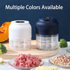 A white and blue mini USB rechargeable electric food chopper is shown with chopped herbs and garlic on a wooden cutting board