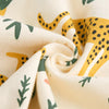 A close-up of a cream fabric with yellow and green animal print patterns, folded to show the textile texture.