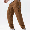 A man wearing brown cargo joggers and a white shirt stands, showing the fit of the pants.