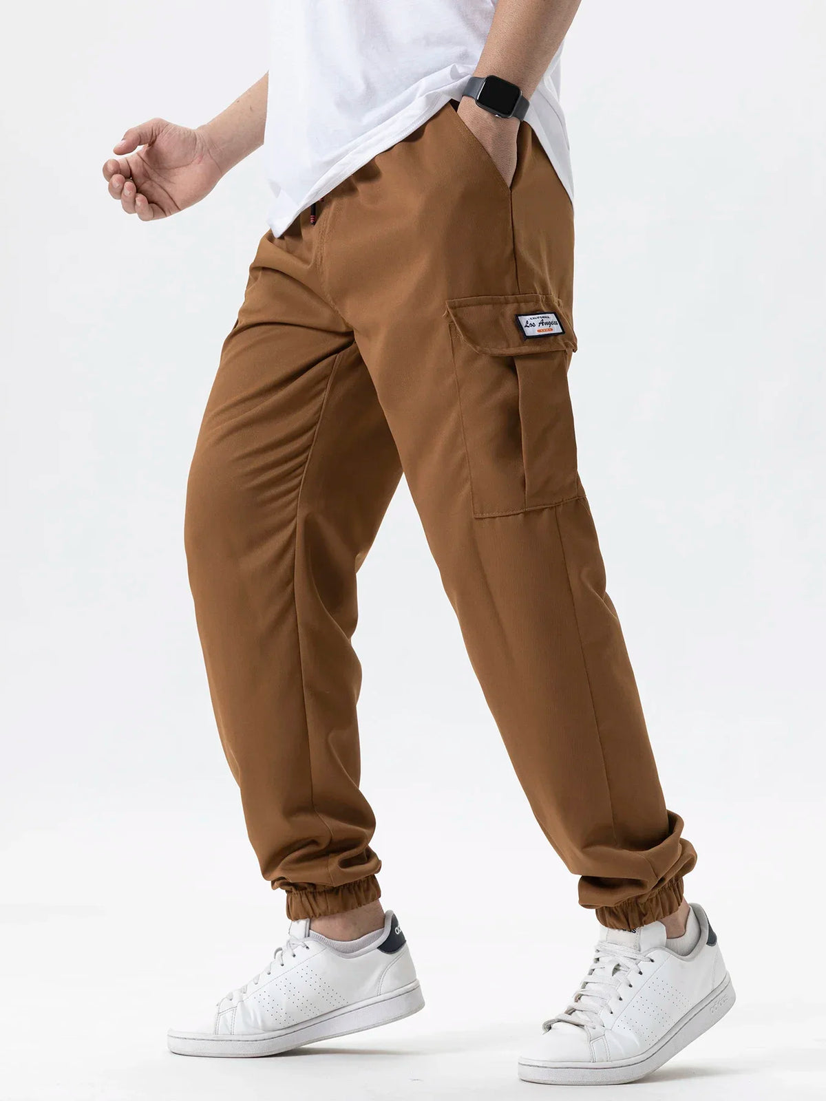 A man wearing brown cargo joggers and a white shirt stands, showing the fit of the pants.