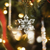 Gjennomsiktig akryl snøfnugg-ornament hengende på et juletre med varme bokeh-lys.