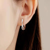 Primer plano de la oreja de una mujer con pendientes de aro trenzados de circonita y plata de ley.