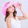 A woman models a pink wide brim organza sun hat with ruffled mesh against a light gray background.