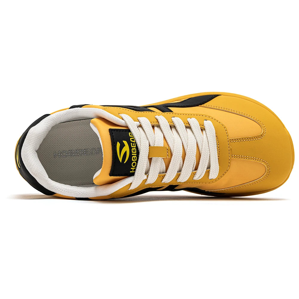 Ein gelber und schwarzer minimalistische Barfußsneaker von der Seite mit weißen Schnürsenkeln.