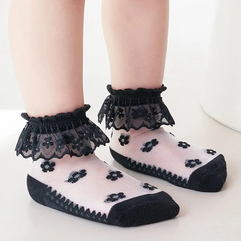 A pair of black lace ruffle ankle socks for a baby girl displayed on a white surface.