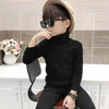 A young boy wearing a black turtleneck sweater and sunglasses is seated in front of a white cabinet.