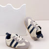 A pair of baby first walker shoes with a grey and white striped pattern are shown next to a white card.