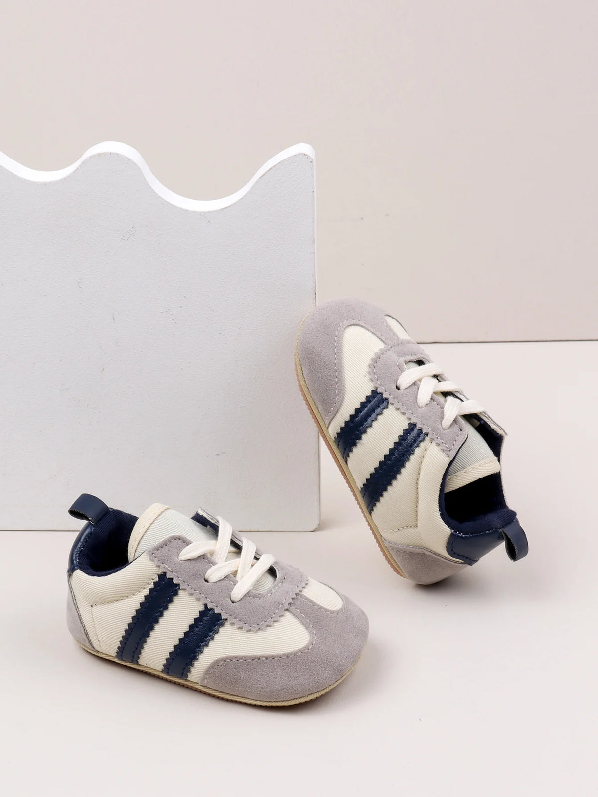 A pair of baby first walker shoes with a grey and white striped pattern are shown next to a white card.