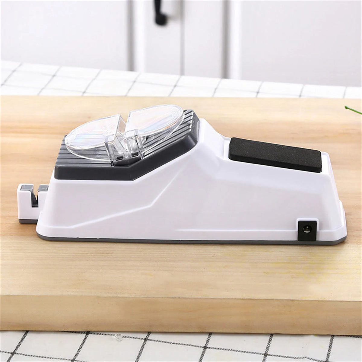 A white electric knife sharpener with a clear protective cover rests on a wooden cutting board.