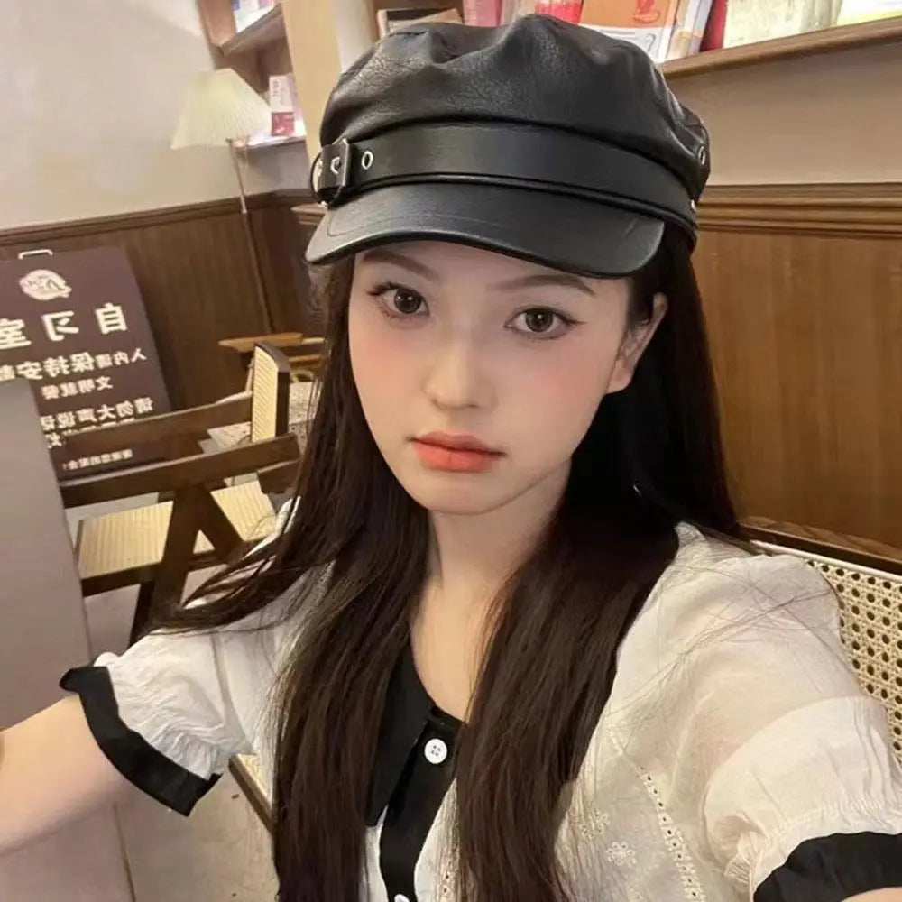 A young woman wearing a black PU leather beret hat and a white blouse indoors.