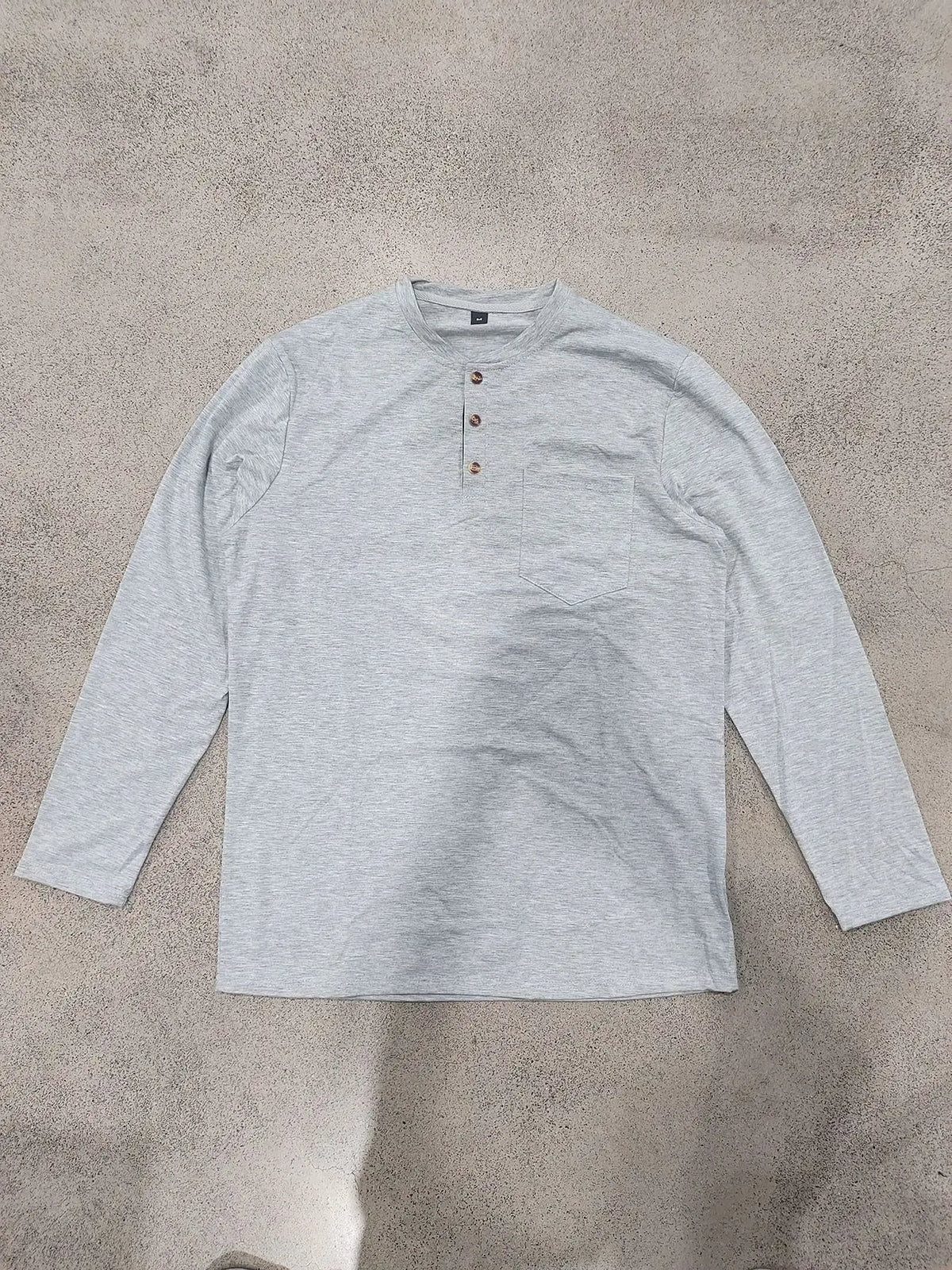 A light gray men's casual long-sleeve shirt with a collar and chest pocket lying flat on a textured surface.
