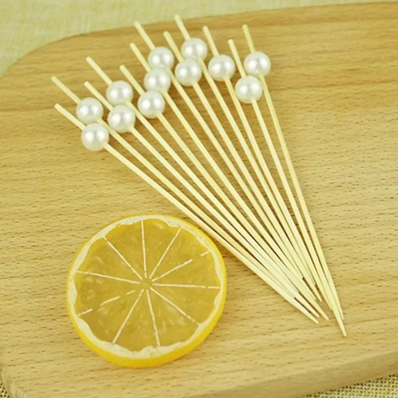 Elegant pearl bamboo skewers arranged on a wooden board next to a slice of lemon.