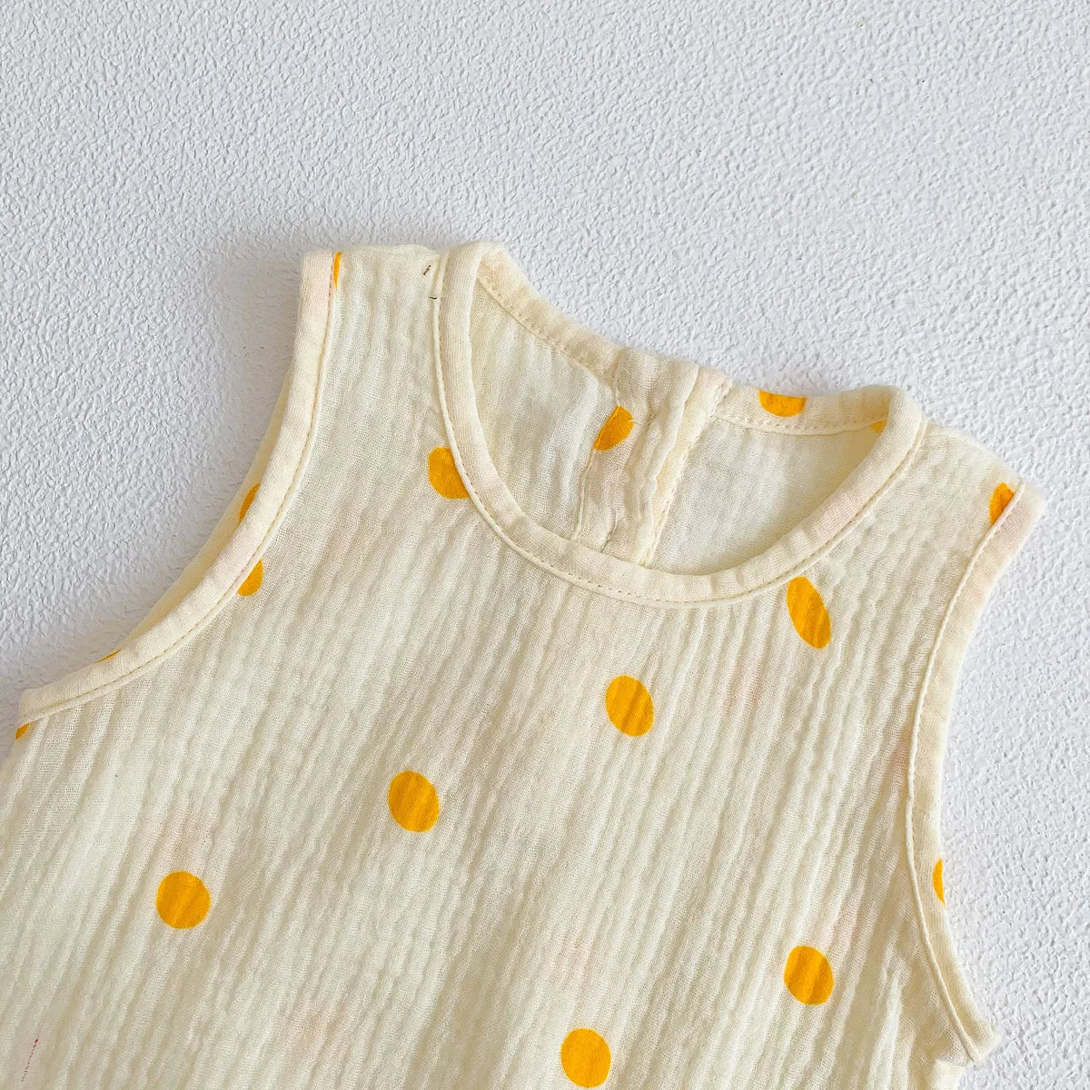 A cream-colored baby cotton sleeveless jumpsuit bodysuit set with scattered orange polka dots.