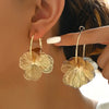 Golden double-layer hollow flower hoop earrings worn by a woman's ear.