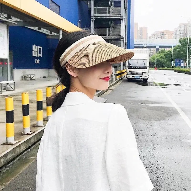 A woman wearing a white coat and a woven straw sun hat is standing on an asphalt road next to a blue building.