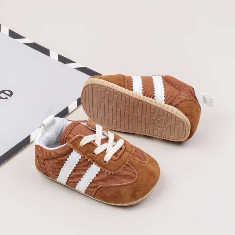 A pair of brown baby first walker shoes with white stripes and an anti-slip TPR sole are shown next to a box.