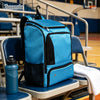 A bright blue sports backpack resting on a bench in a gym setting.