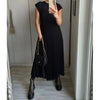 A woman wearing a black sleeveless pleated midi dress and black boots standing in a hallway.