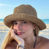 A young woman wearing a wide-brimmed woven straw hat outdoors near the sea.