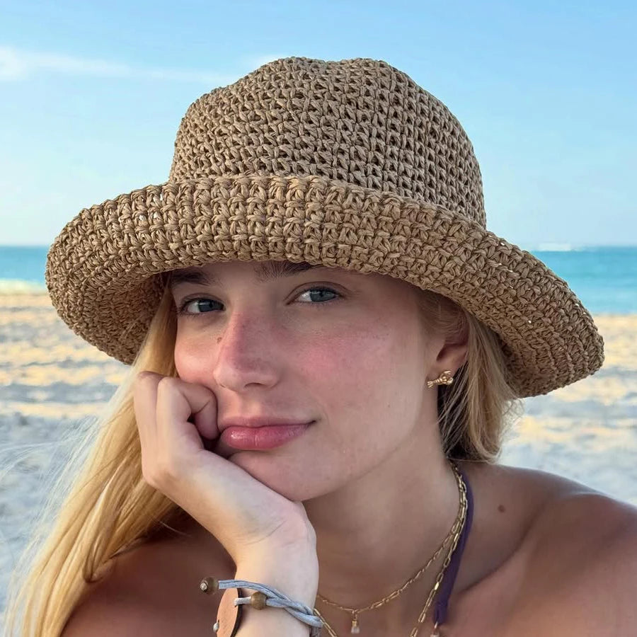 A young woman wearing a wide-brimmed woven straw hat outdoors near the sea.