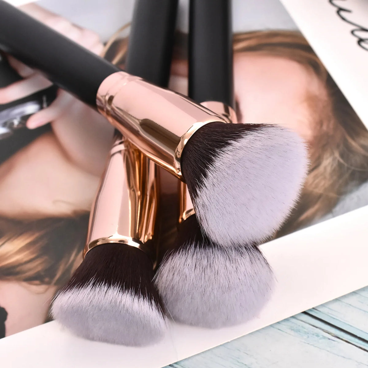 A close-up of a professional makeup brush with pink and gray bristles shown against a light background.
