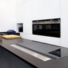 A black silicone stove protector mat is placed on a dark countertop in front of modern kitchen cabinetry.