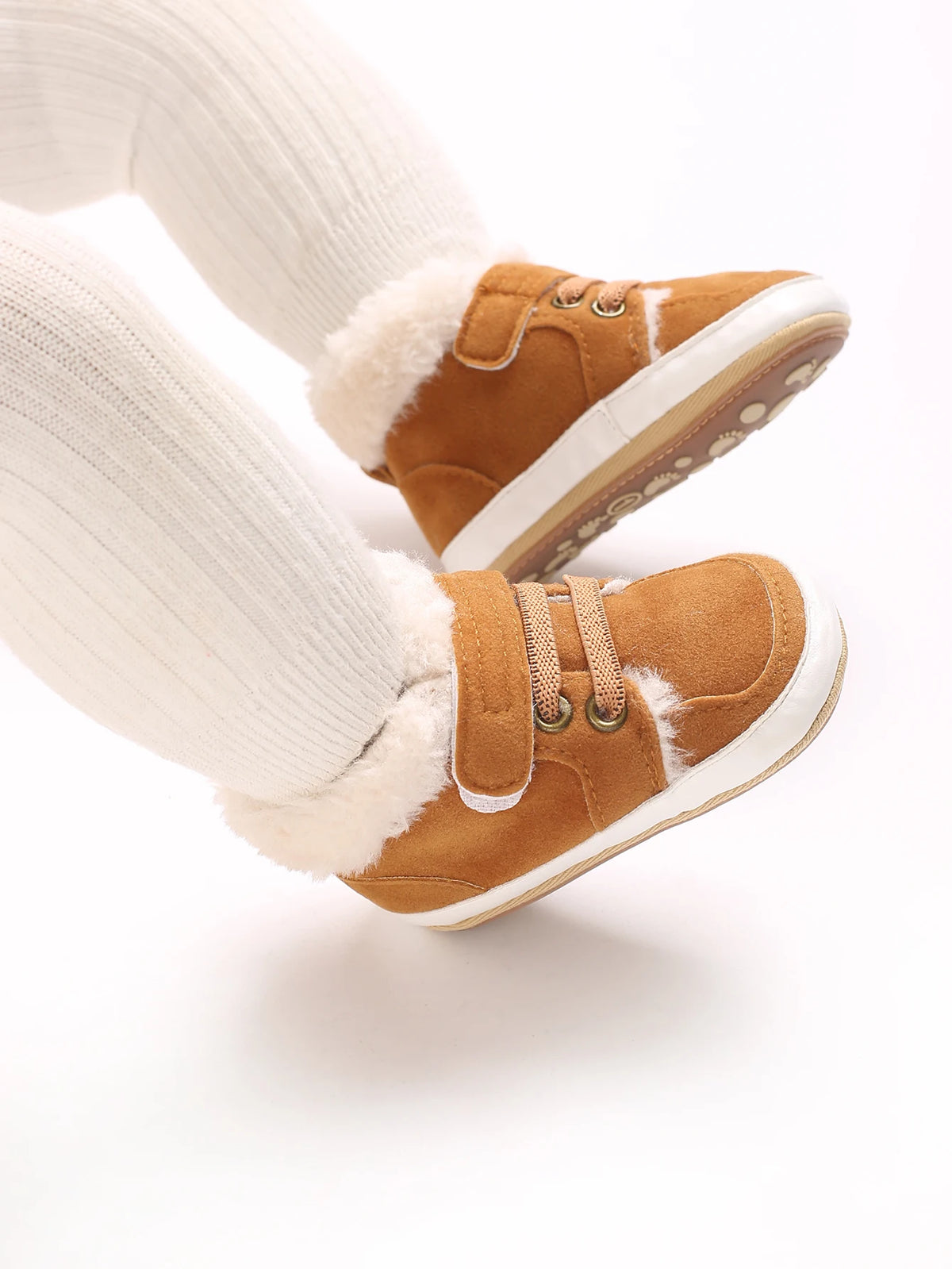 A pair of tan suede baby winter snow boots with white fuzzy trim and white socks.