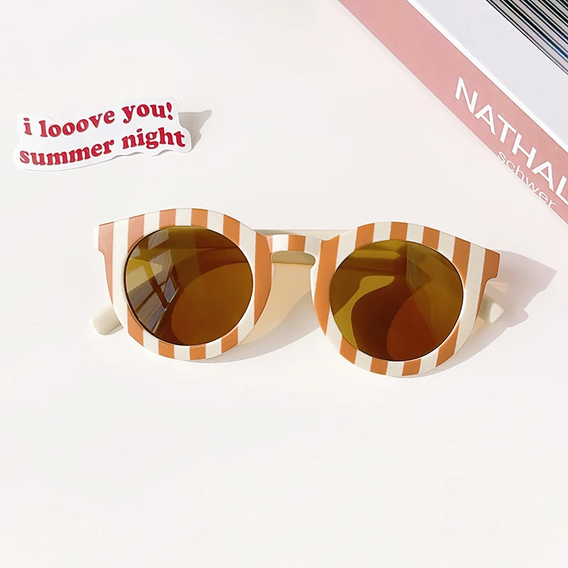 A pair of orange-tinted sunglasses with a striped frame resting on a white surface.