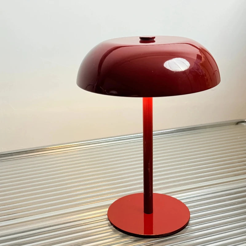 A modern table lamp with a glossy maroon shade and a slender red stand on a silver striped surface.