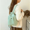 A woman wearing a light mint green mini backpack and a cream knit sweater.