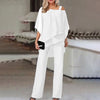 En kvinne modellerer et hvitt to-delt sett med off-shoulder topp og brede bukser.