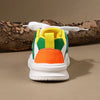 A pair of kids' breathable casual sneakers with hook-and-loop closure in white, green, and orange colors resting on a piece o