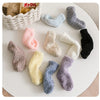 A collection of nine fuzzy socks in various pastel and dark colors arranged on a white surface.