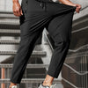 A muscular man wearing black high-stretch joggers with a drawstring and zipper pockets, standing in an indoor setting.