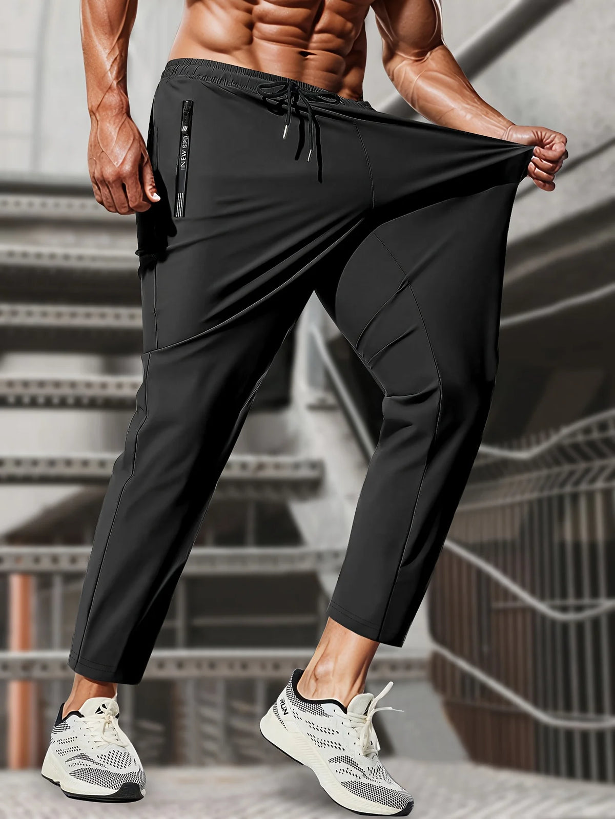 A muscular man wearing black high-stretch joggers with a drawstring and zipper pockets, standing in an indoor setting.