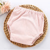 Pink organic cotton baby training pants resting on a woven natural fiber tray