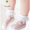 A pair of white lace ruffle ankle socks for a baby girl shown on a leg.
