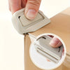 A hand is using a white retractable ceramic blade cutter with a magnetic lock on a light brown box.