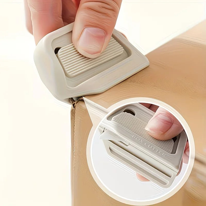 A hand is using a white retractable ceramic blade cutter with a magnetic lock on a light brown box.
