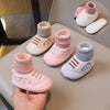 A hand holds a pair of pink knit baby booties with bear designs, shown next to other colored booties.
