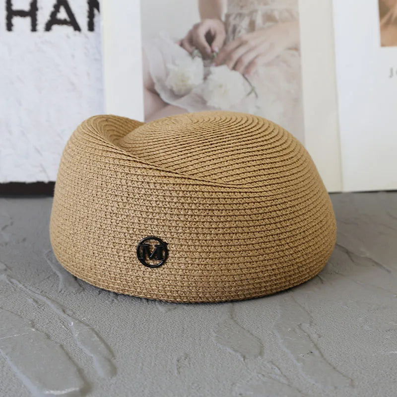A beige straw pillbox sun hat with a wide brim resting on a gray surface.