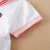 A close-up of a white kids' summer cotton dress with a pink turn-down collar and red embroidery detail.